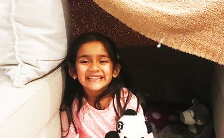 A girl smiling inside a homemade tent.