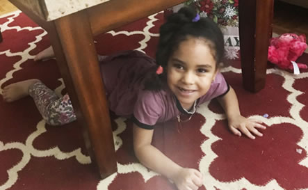 A girl smiling underneath a table.